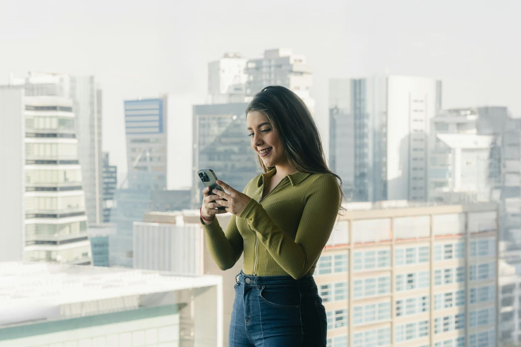 Gestora no terraço olhando o celular, com prédios ao fundo