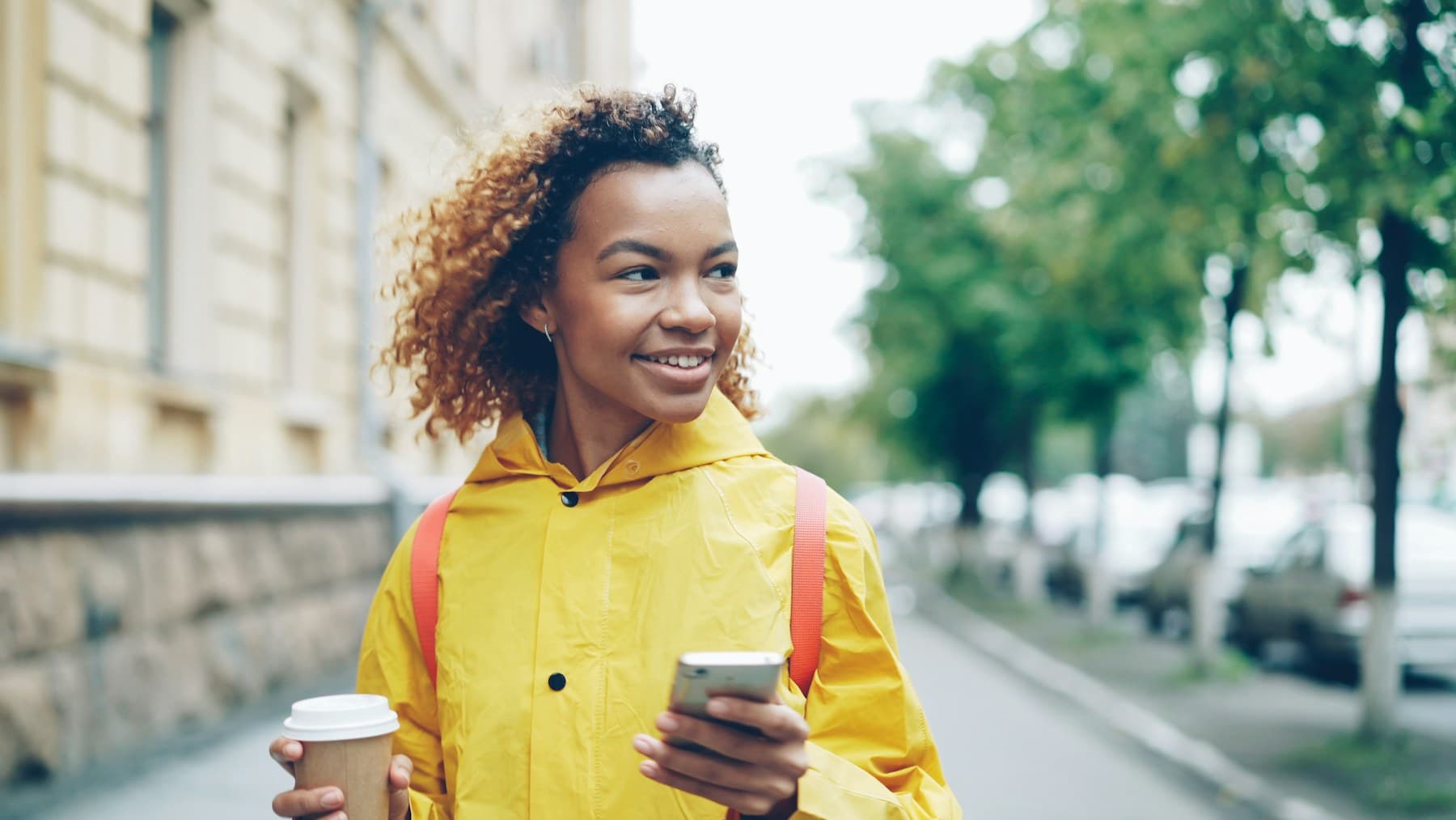 Moradora sorrindo na rua, com o celular na mão